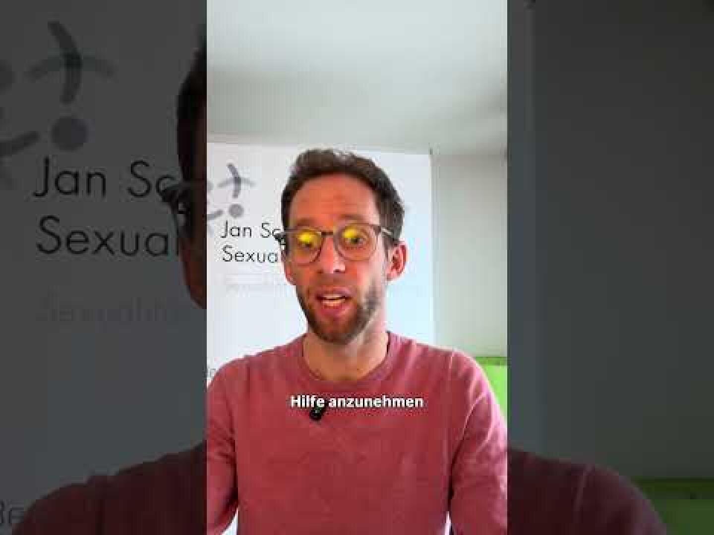 Ein Mann mit Brille und Bart spricht vor einem Banner, auf dem teilweise "Sexual" und "Jan S." zu lesen ist. Die Untertitel am unteren Bildrand lauten "Hilfe annehmen".