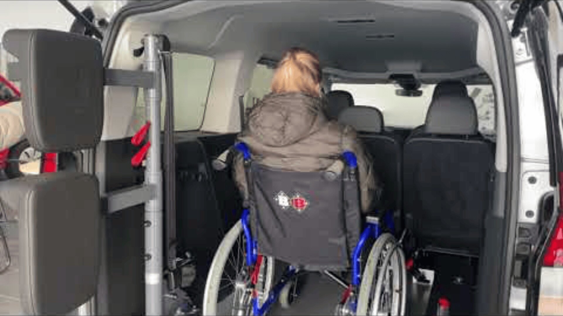 Eine Person im Rollstuhl blickt nach vorne in einen Lieferwagen mit offener Hecktür, der ein für Rollstuhlfahrer konzipiertes Fahrzeuginnere zeigt.