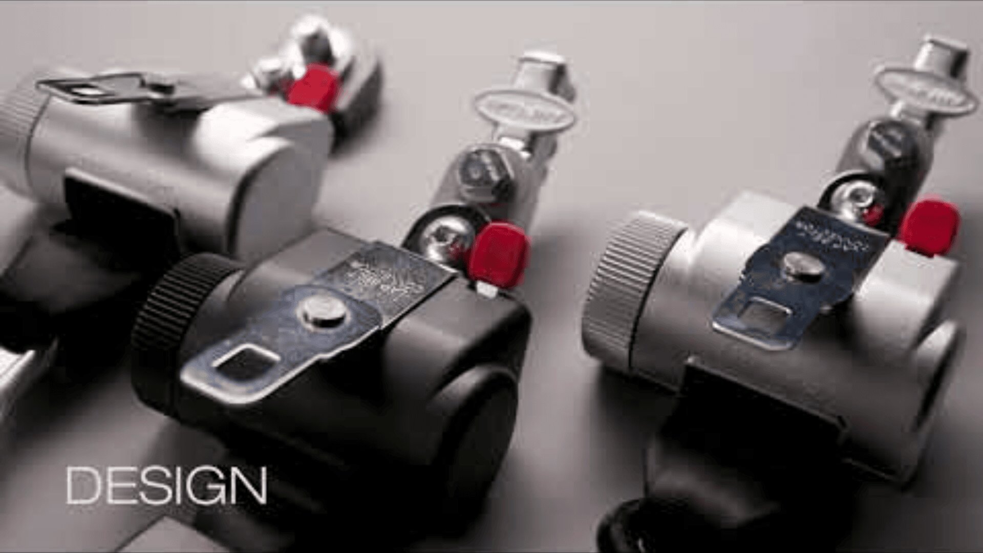 Nahaufnahme von drei Metallschlössern mit eingesteckten Schlüsseln, zwei in Silber und eines in Schwarz, auf einer grauen Fläche. Das Wort DESIGN erscheint in weißer Schrift in der unteren linken Ecke.
